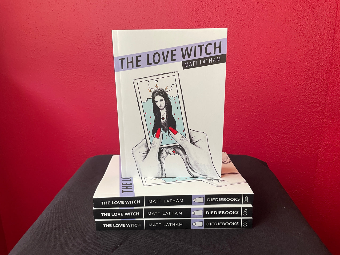 Stack of books titled 'The Love Witch' by Matt Latham against a red background