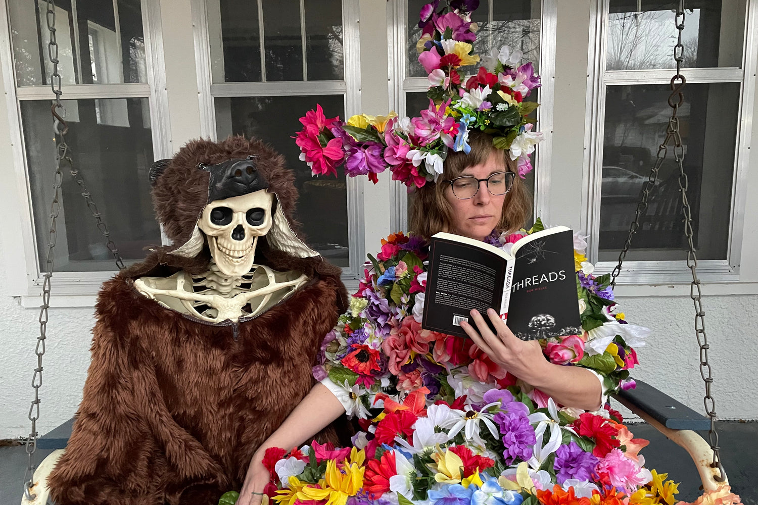 shot of Rachel Kempf dressed as Dani from Midsommar reading a DieDieBook next to a skeleton in a bear suit