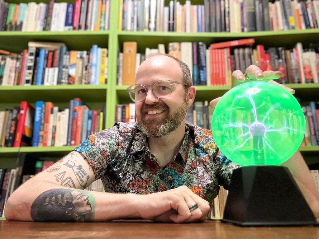 Photo of Anthony Bowman sitting next to a  green glowing electricity orb in front of wall-size bookshelves
