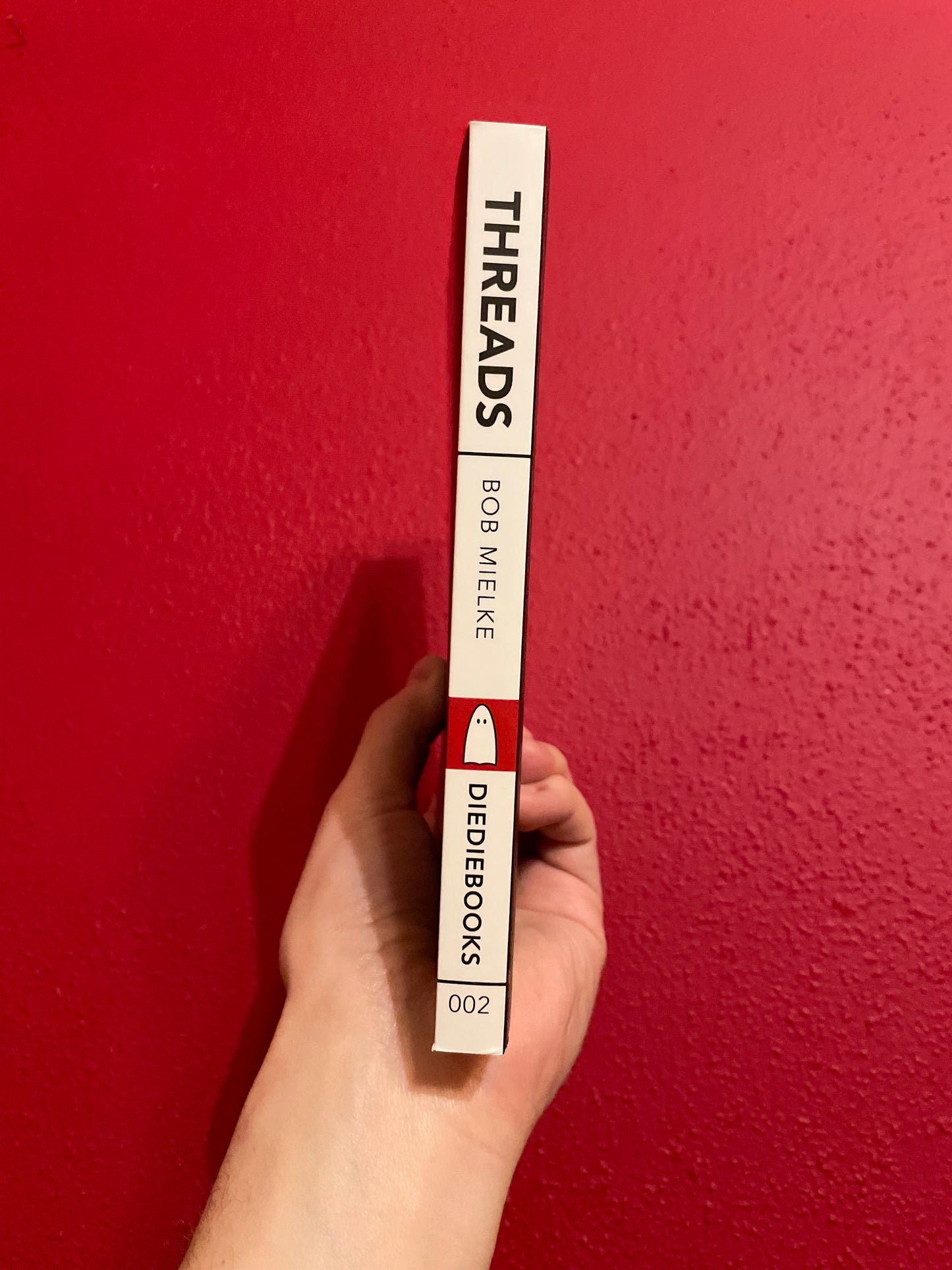 Image of a hand holding up a Threads book to show the black-and-white spine